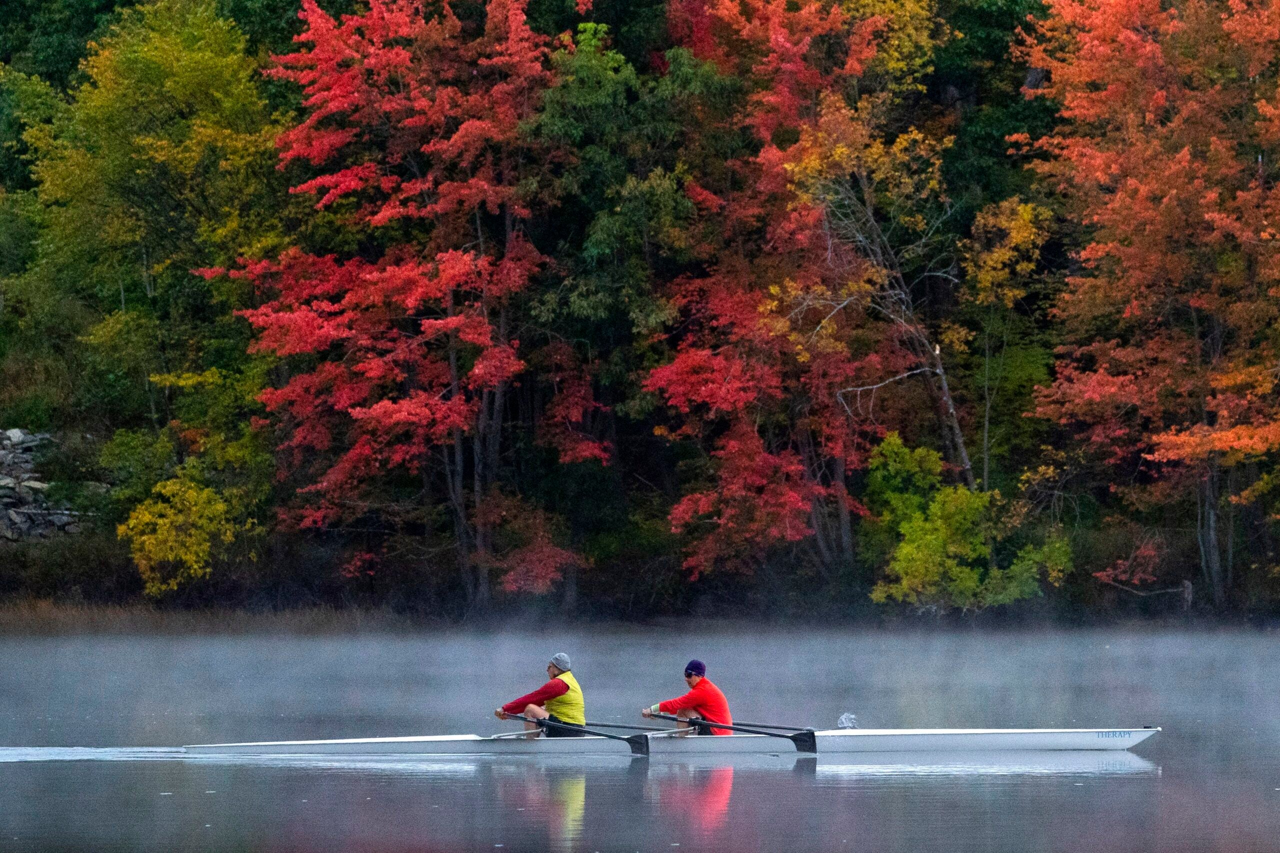 A pair of rowers glide on the Androscoggin River past fall foliage in Brunswick, Maine.