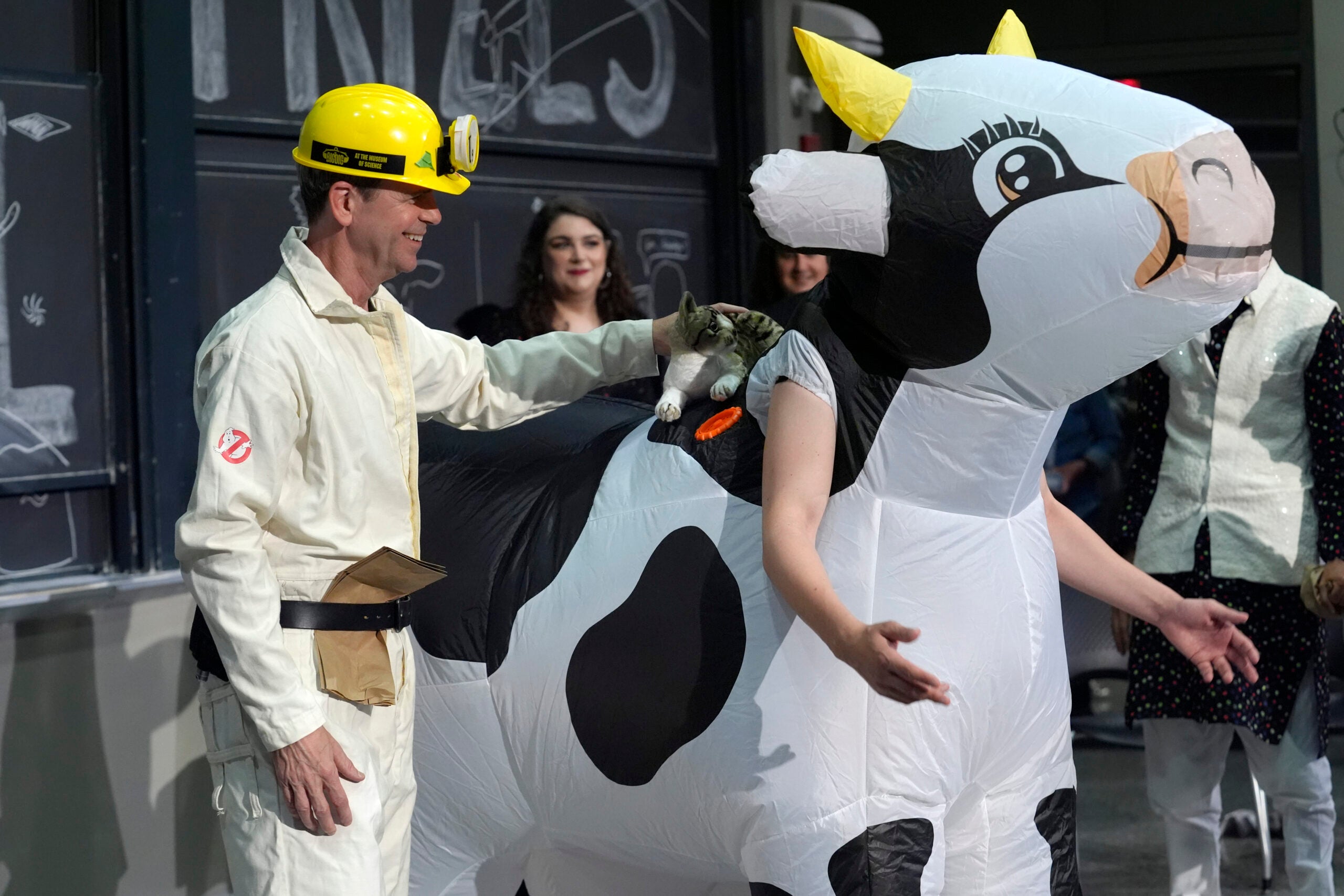 An artist places a stuffed cat on an inflatable cow.