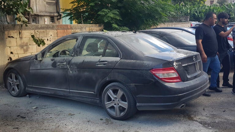 Lebanese security officers stand next of a partly damaged car after what is believed to be the result of a walkie-talkie exploding inside it, in the southern port city of Sidon, Lebanon.