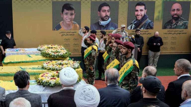 Hezbollah fighters salute as they stand next to the coffins of four victims.