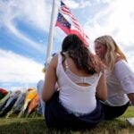 Two students view a memorial as the flags fly half-staff after a shooting Wednesday at Apalachee High School, Thursday, Sept. 5, 2024, in Winder, Ga.