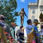 A crowd surrounds the newly-unveiled statue of Christa McAuliffe at the New Hampshire Statehouse, Monday, Sept. 2, 2024, in Concord, N.H.