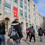 Students and passers-by carry book bags as they walk past an entrance to Boston University College of Arts and Sciences, in Boston.