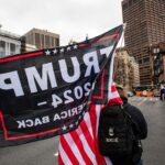 A man carrying a US Flag and a Trump 2024 flag in Boston, Massachusetts on January 5, 2022.