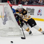 Brad Marchand wraps around the net with the puck as Avalanche's Oliver Kylington pursues.