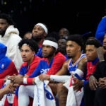 Joel Embiid and Paul George watch a 76ers-Bucks game from the bench.
