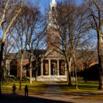 A pedestrian walks through Harvard University’s campus in Cambridge, Mass.