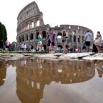 Tourists walk by the ancient Roman Colosseum as it's reflected in a puddle, in Rome.