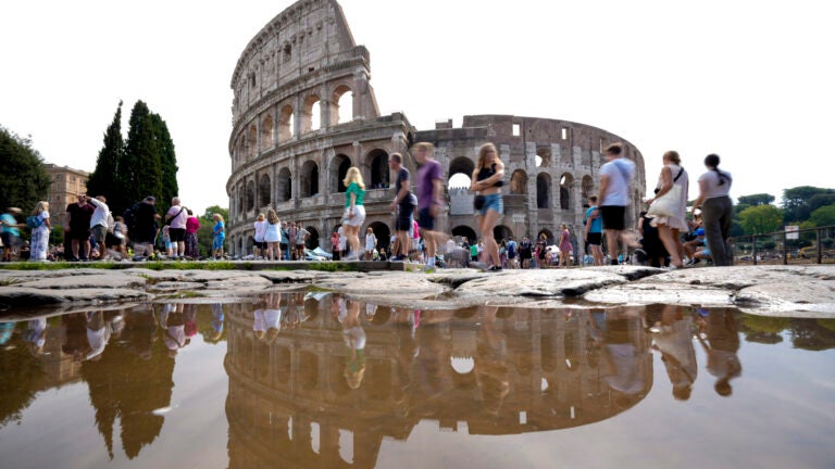 Tourists walk by the ancient Roman Colosseum as it's reflected in a puddle, in Rome.