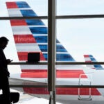 A passenger talks on the phone with American Airlines jets parked behind him.
