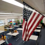 An American flag hangs in a classroom as students work on laptops.