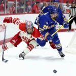 Ohio St. forward Aiden Hansen-Bukata and Lake Superior St. forward John Herrington skate after the puck.