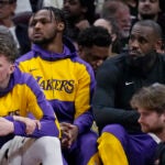 Bronny James and LeBron James watch from the bench.