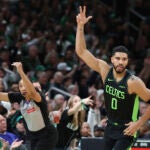 Jayson Tatum signals three after hitting an outside shot during a game against the Raptors.