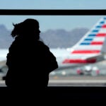 A woman waits for her flight as an American Airlines jet passes by at Sky Harbor airport.