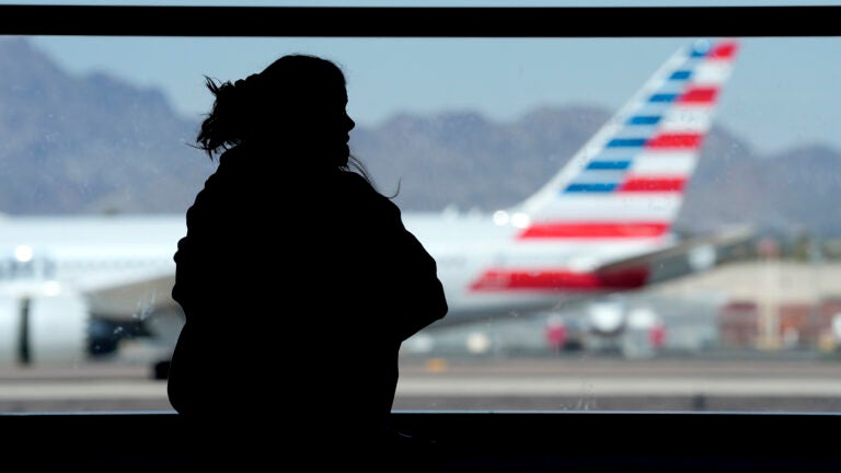 A woman waits for her flight as an American Airlines jet passes by at Sky Harbor airport.