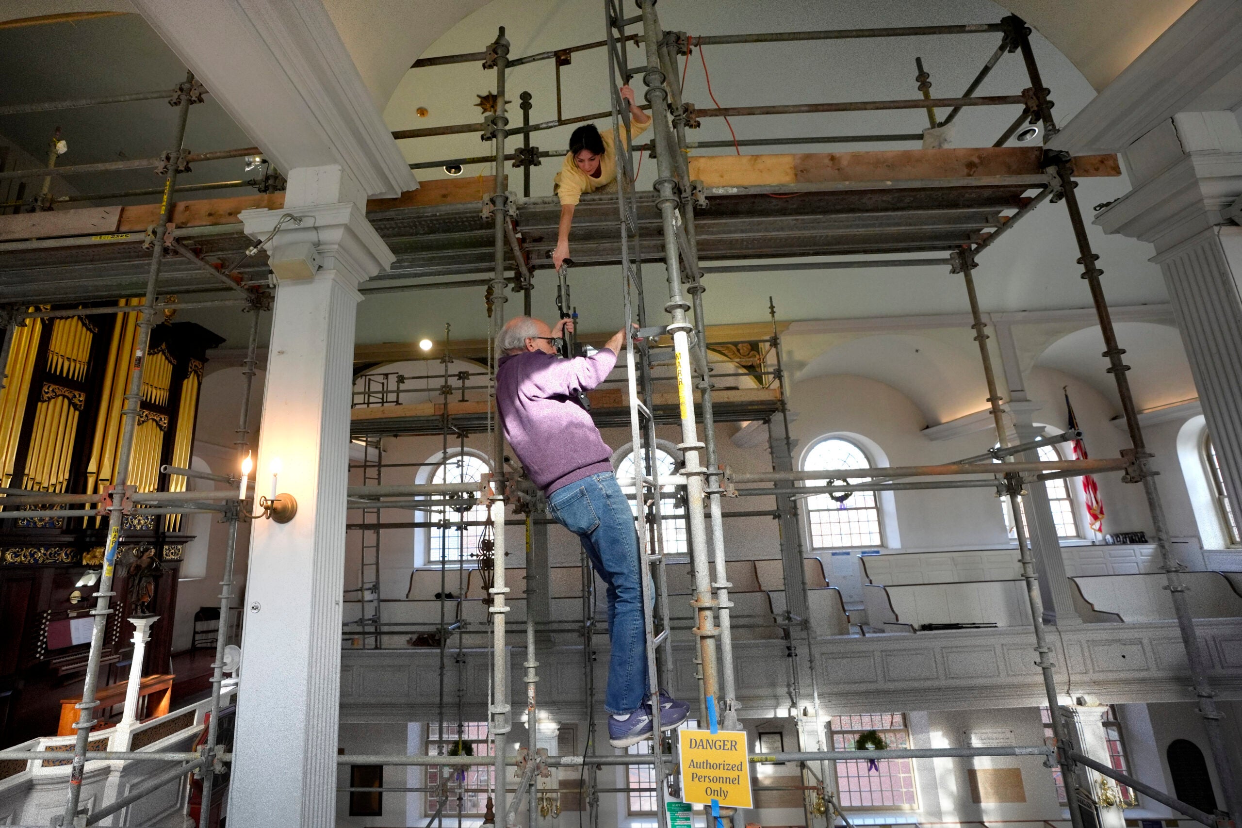 Conservator Corrine Long, of Dover, N.H., top, hands equipment to conservator Gianfranco Pocobene, of Malden, Mass., center, as they climb down scaffolding. 