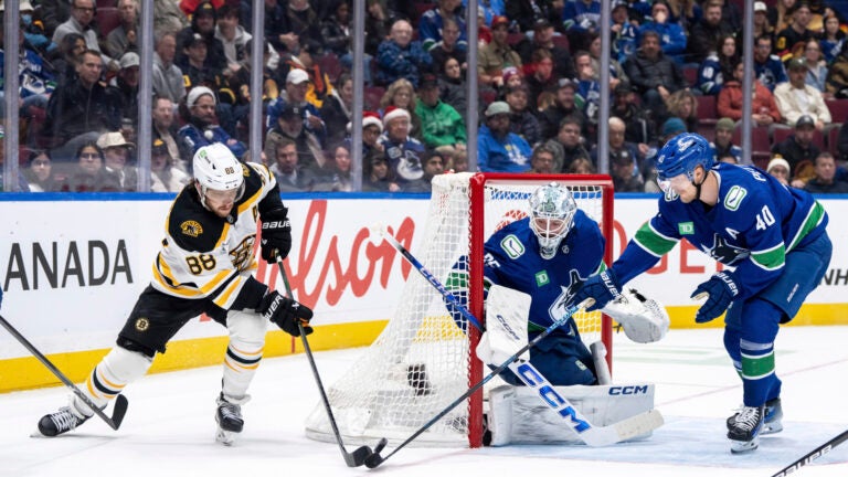 Boston Bruins' David Pastrnak (88) and Vancouver Canucks' Elias Pettersson (40) vie for the puck as goaltender Thatcher Demko (35) watches during the second period of an NHL hockey game in Vancouver, British Columbia, Saturday, Dec. 14, 2024.