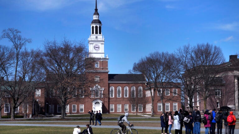 A bicyclist passes a college tour group outside the Baker Library at Dartmouth College, April 7, 2023, in Hanover, N.H.