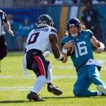 Trevor Lawrence begins to slide down as Azeez Al-Shaair charges forward.