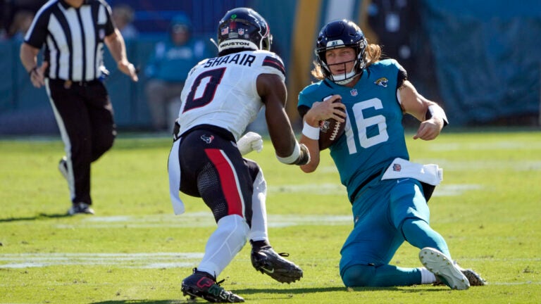 Trevor Lawrence begins to slide down as Azeez Al-Shaair charges forward.