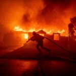 A firefighter battles the Palisades Fire as it burns a structure.