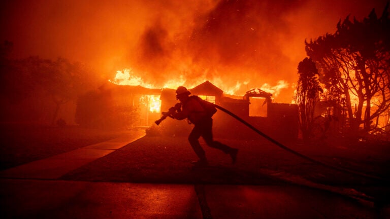 A firefighter battles the Palisades Fire as it burns a structure.