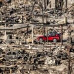 A car drives past homes and vehicles destroyed by the Palisades Fire.