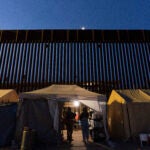 Volunteers talk in a tent along a border wall separating Mexico from the United States.
