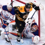 Boston Bruins right wing David Pastrnak (88) steps over Edmonton Oilers goaltender Stuart Skinner while chasing the puck against defenseman Brett Kulak (27) during the first period of an NHL hockey game, Tuesday, Jan. 7, 2025, in Boston.
