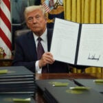 President Donald Trump holds up an executive order commuting sentences for people convicted of Jan. 6 offenses in the Oval Office of the White House, Monday, Jan. 20, 2025, in Washington.