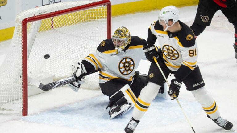 Boston Bruins defenseman Nikita Zadorov (91) looks over his shoulder to watch goaltender Jeremy Swayman, left, swing at the puck entering the net for a goal during first-period NHL hockey game action against the Ottawa Senators, Thursday, March 13, 2025, in Ottawa, Ontario.