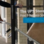 A UPS driver enters a United Parcel Service store with packages.