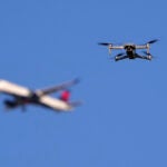 FILE - A drone hovers in airspace outside the safety perimeter surrounding St. Louis Lambert International Airport as an airliner approaches for a landing on March 10, 2025.