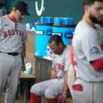 Alex Cora stands while talking to Rafael Devers, who is seated on the dugout bench.
