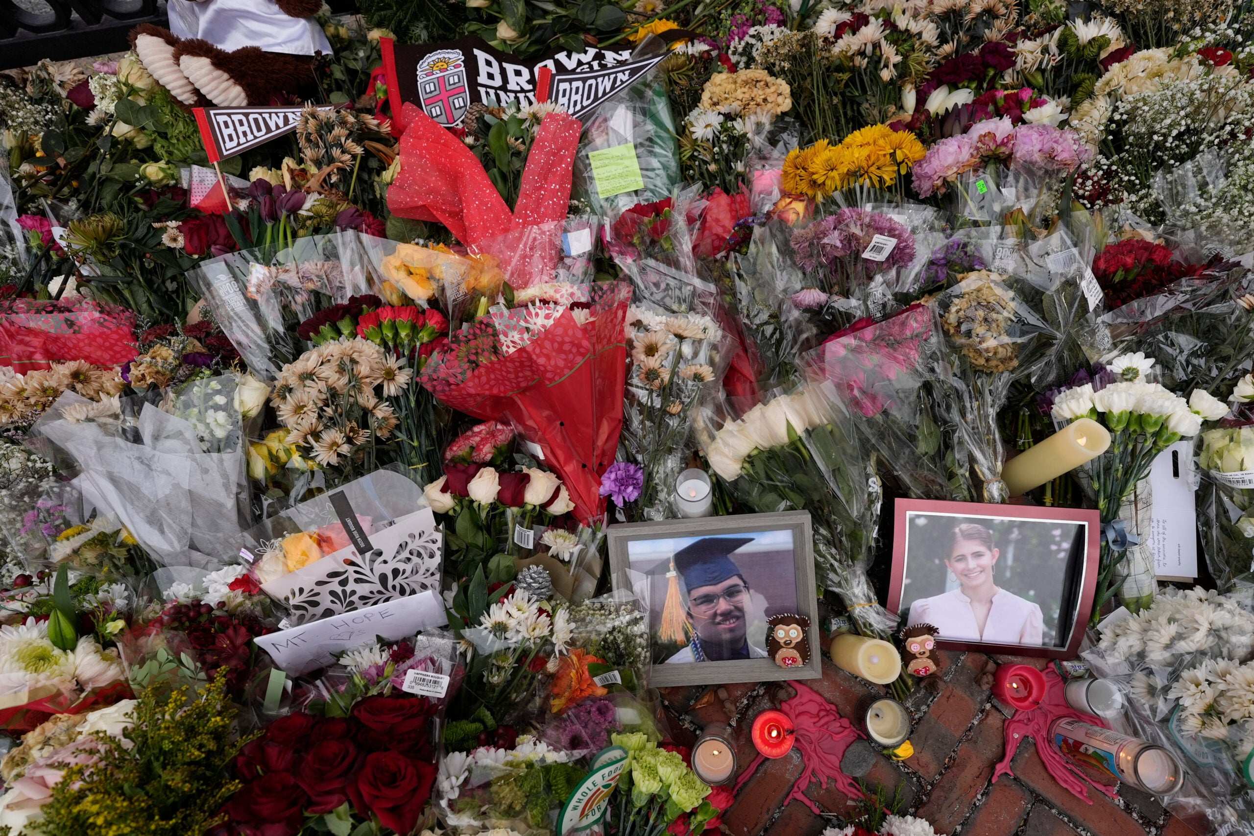 Photos of Brown University shooting victims Mukhammad Aziz Umurzokov, left, and Ella Cook, are seen amongst flowers at a makeshift memorial at the school's Van Wickle Gate, Dec. 17, 2025, in Providence, R.I. 