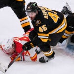 Calgary Flames center Connor Zary (47) is knocked to the ice by Boston Bruins defenseman Jonathan Aspirot (45) during the second period of an NHL hockey game, Thursday, Jan. 8, 2026, in Boston.