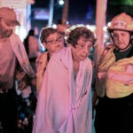 A resident of the Gabriel House Assisted Living facility on Oliver Street in Fall River is assisted in a nearby parking lot late Sunday night after a fire displaced several residents and caused injuries.