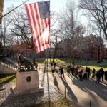 People take photos near a John Harvard statue on the Harvard University campus,