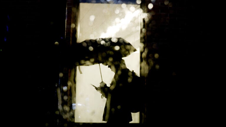 A pedestrian checks his phone as he takes cover under an umbrella as rain falls in Boston.