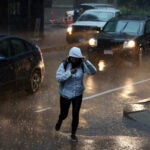 A pedestrian navigates Kilby Street during heavy rain in downtown Boston.
