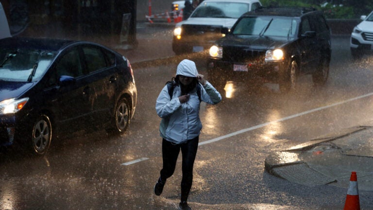 A pedestrian navigates Kilby Street during heavy rain in downtown Boston.