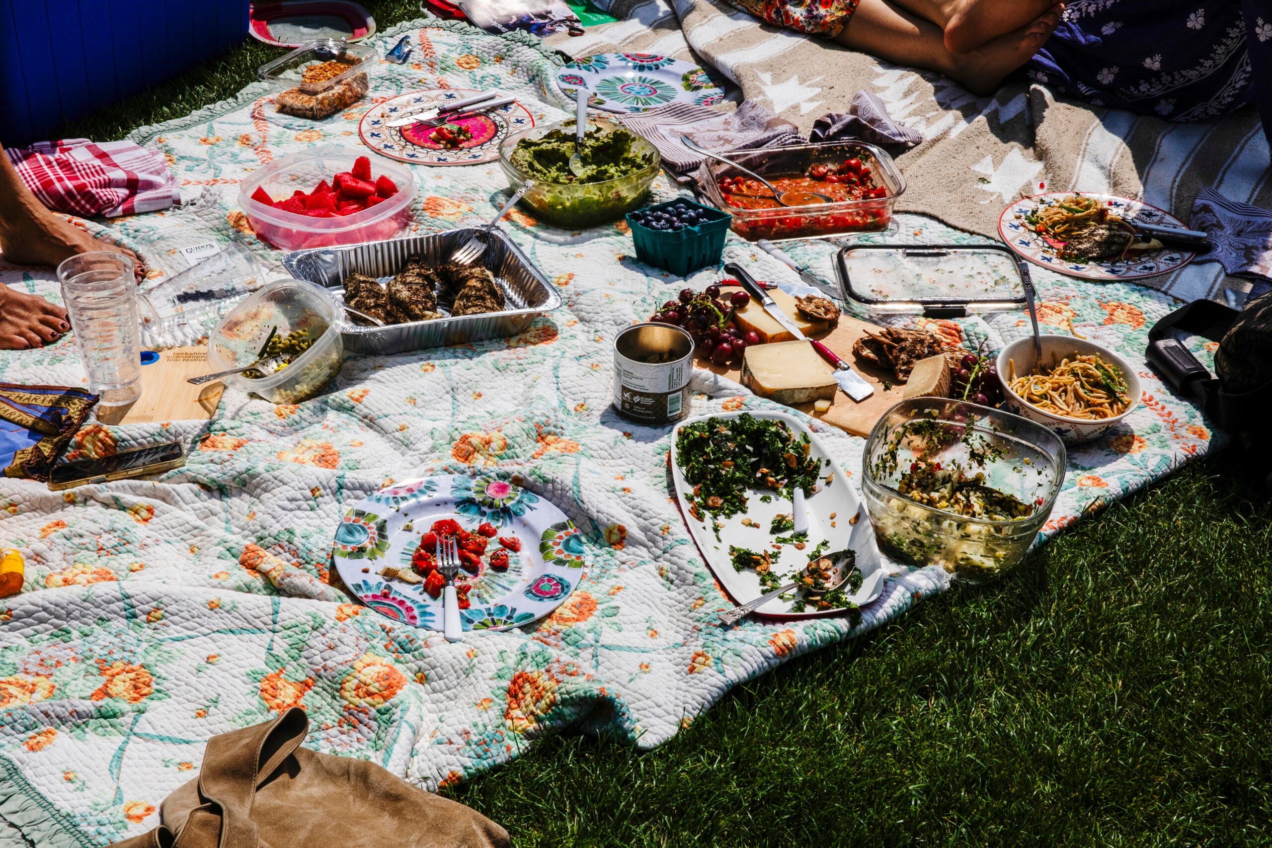 A picnic blanket full of food sits on the lawn.