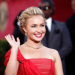 A woman in a red dress waves on the red carpet.