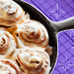 A cast iron pan filled with cinnamon rolls against a purple background