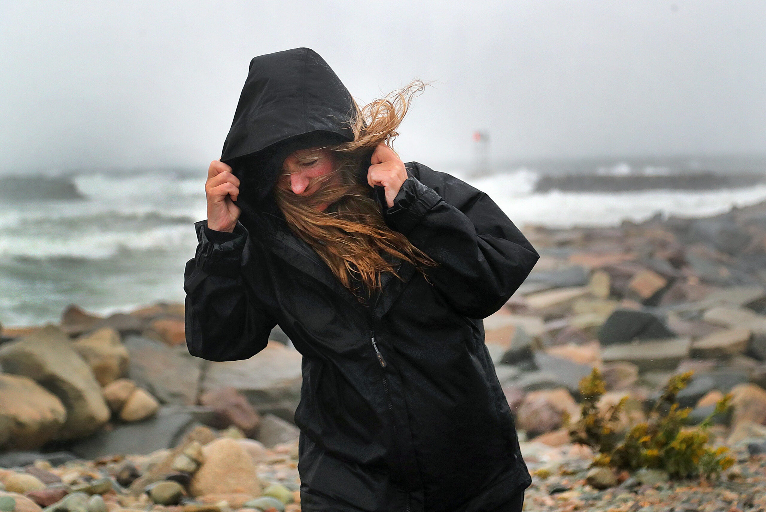A woman in a black raincoat braces in the wind.