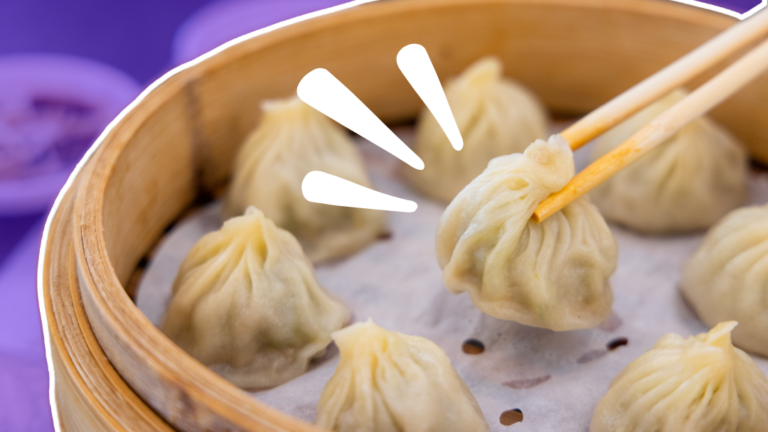 A pair of chopsticks picking up a soup dumpling from a dim sum basket with paper at the bottom. The basket is outlined in white, and the background of he table is faded to purple. There are three white accent marks next to the soup dumpling that is being picked up.